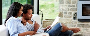 Young couple sitting in their living room and reading about the steps to build a solid financial foundation