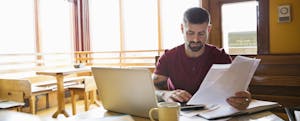 Man at desk with laptop going through financial papers.