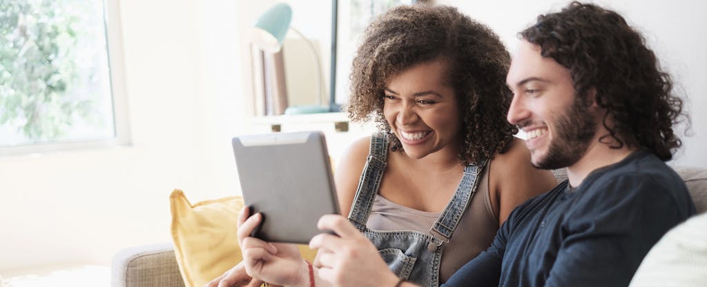Man and woman sitting on a couch together, looking at a tablet