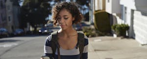 Woman walking up a hill in a city, looking at her phone