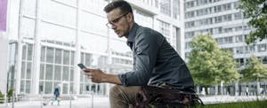 Man sitting outside downtown office building, looking up Wise Loans on his cellphone