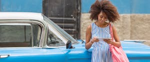 best-auto-loan-rates_909565786 Smiling woman looking at tablet while leaning on a car
