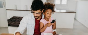 Father and daughter in kitchen. Daughter is holding calculator and father is trying to figure out how much he needs to retire