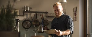 Young man standing in kitchen reading about first time home purchasing.