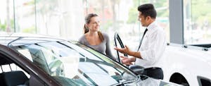 A salesman shows a young woman a new car at a dealership.