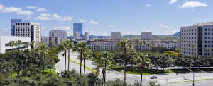 Aerial view of the downtown Irvine, California skyline with palm trees in the foreground and a blue sky overhead..