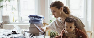 why-is-rent-so-expensive Woman sitting at home with her baby, paying her rent on her computer