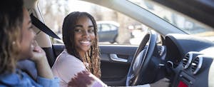 Mom and daughter in a car with the daughter behind the wheel