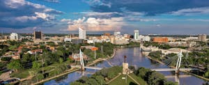 Aerial view of the downtown Wichita, Kansas skyline against a blue sky, with the Arkansas River in the foreground