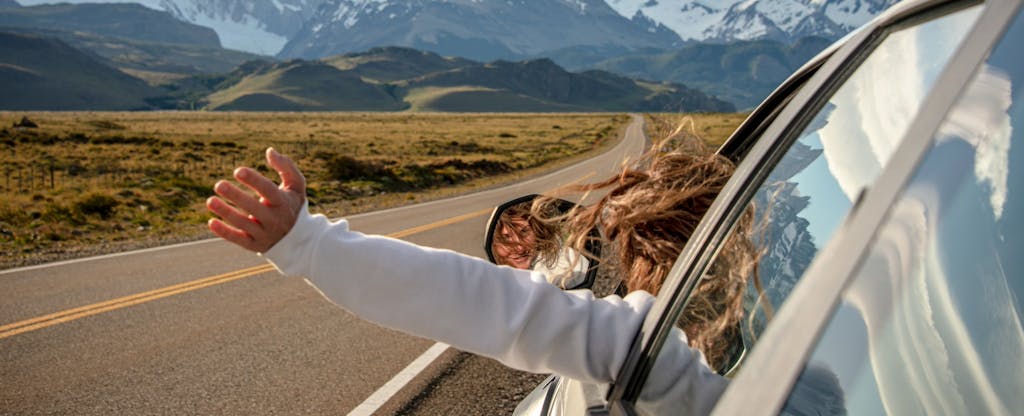 Woman with arm out car window, driving to the mountains.
